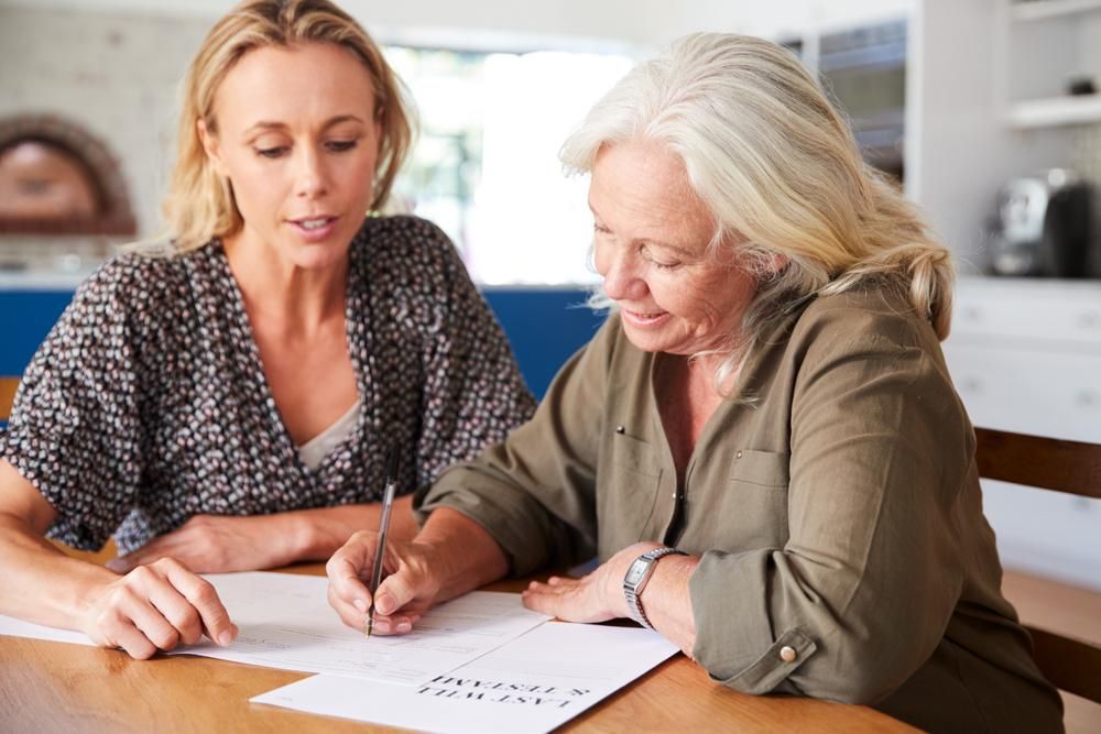 Two Women Are Sitting At A Table Writing On A Piece Of Paper — Howells & Co Legal & Conveyancing In Port Stephens, NSW