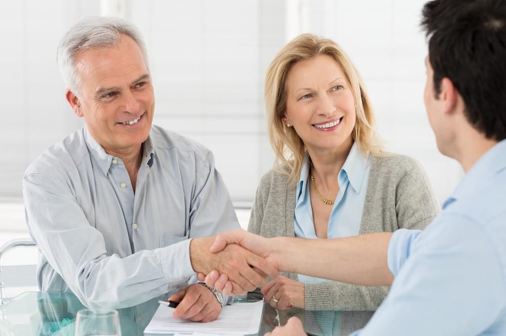 A Man And Woman Are Shaking Hands With A Man While Sitting At A Table — Howells & Co Legal & Conveyancing In Coffs Harbour, NSW