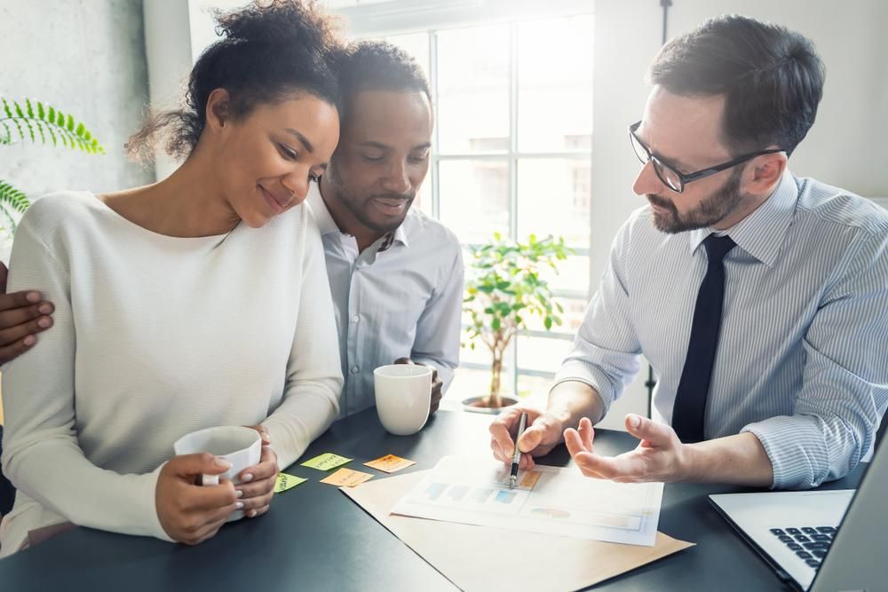 A Man Is Sitting At A Table With A Woman And A Man — Howells & Co Legal & Conveyancing In Cessnock, NSW