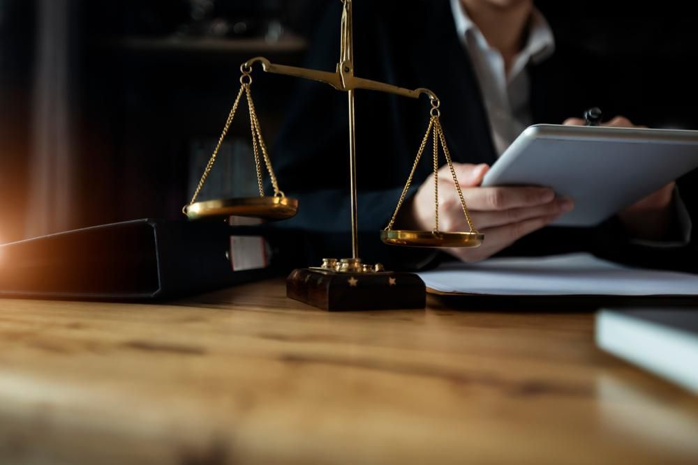 A Woman Is Sitting At A Table With A Scale Of Justice And A Tablet — Howells & Co Legal & Conveyancing In Albury, NSW