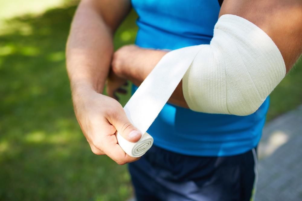 A Man Is Wrapping His Elbow With A Bandage — Howells & Co Legal & Conveyancing In Cessnock, NSW
