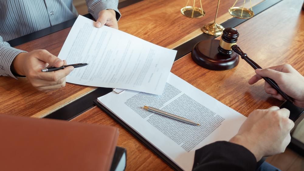 A Couple Of People Are Sitting At A Table With Papers And A Gavel — Howells & Co Legal & Conveyancing In Cessnock, NSW