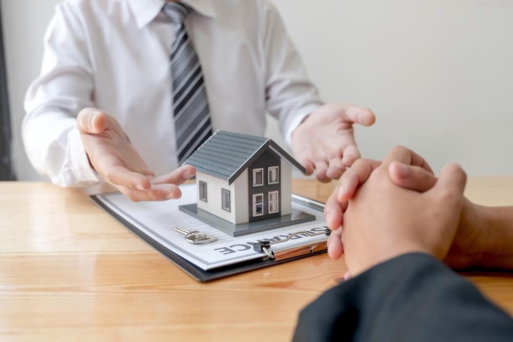 A Man Is Sitting At A Table Holding A Model House — Howells & Co Legal & Conveyancing In Cessnock, NSW
