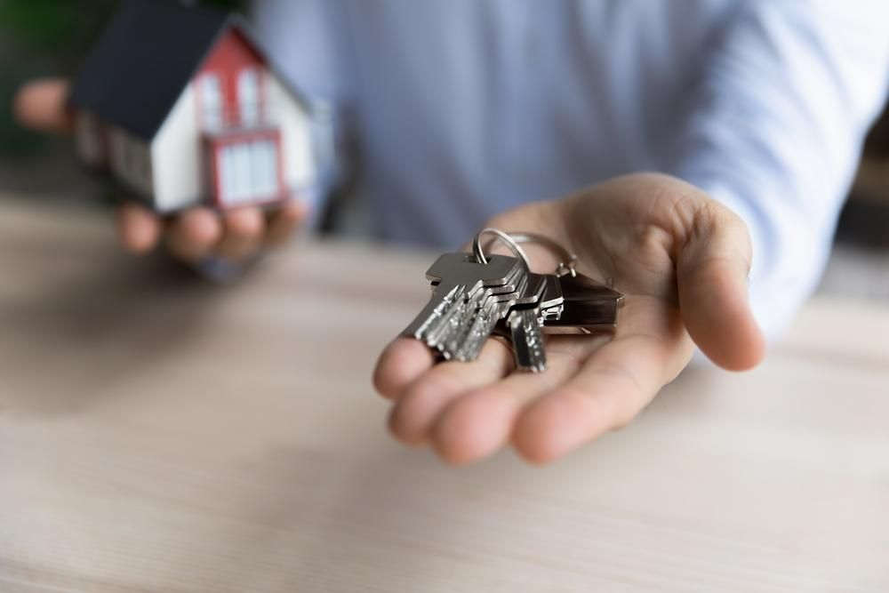 A Person Is Holding A Bunch Of Keys In Their Hand And A Small House In The Background — Howells & Co Legal & Conveyancing In Sydney, NSW