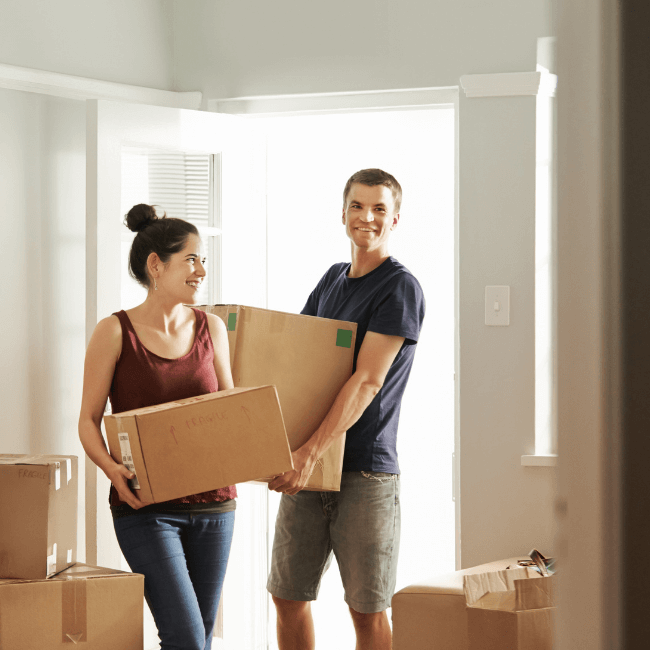A Man And A Woman Are Carrying Boxes Into A New Home — Howells & Co Legal & Conveyancing In Cessnock, NSW