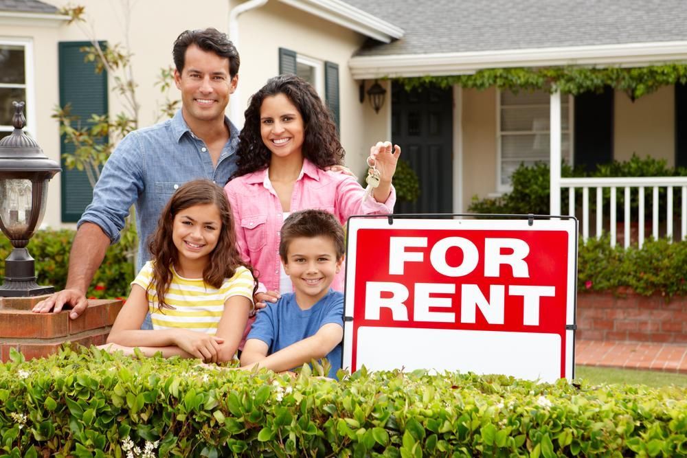 A Family Is Standing In Front Of A House With A For Rent Sign — Howells & Co Legal & Conveyancing In Wyong, NSW