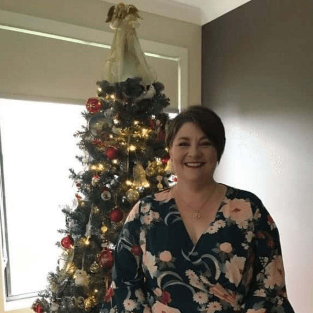 A Woman In A Floral Dress Is Standing In Front Of A Christmas Tree — Howells & Co Legal & Conveyancing In Cessnock, NSW