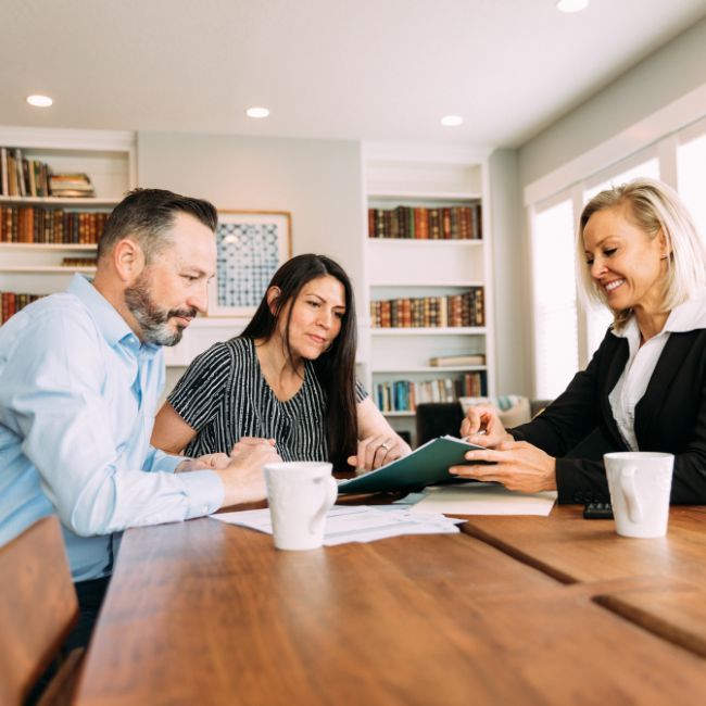 A Man And Two Women Are Sitting At A Table Looking At A Clipboard — Howells & Co Legal & Conveyancing In Cessnock, NSW