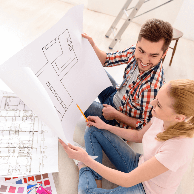 A Man And A Woman Are Sitting On The Floor Looking At A Floor Plan — Howells & Co Legal & Conveyancing In Cessnock, NSW