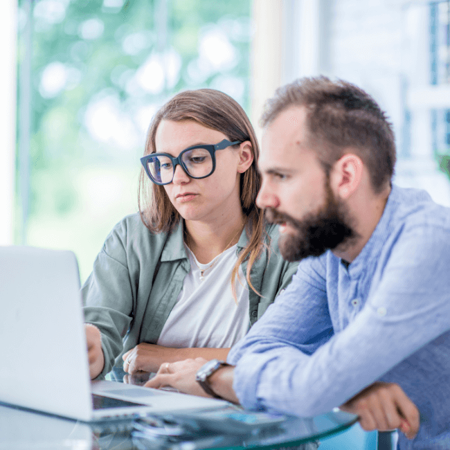 A Man And A Woman Are Sitting At A Table Looking At A Laptop Compute — Howells & Co Legal & Conveyancing In Cessnock, NSW
