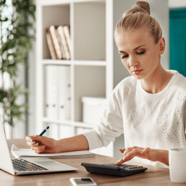 A Woman Is Sitting At A Desk With A Laptop And A Calculator — Howells & Co Legal & Conveyancing In Cessnock, NSW