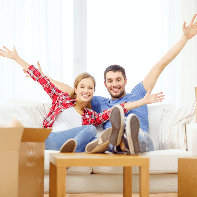 A Man And A Woman Are Sitting On A Couch With Their Arms In The Air — Howells & Co Legal & Conveyancing In Cessnock, NSW