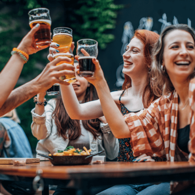 A Group Of People Are Sitting At A Table Toasting With Beer Glasses — Howells & Co Legal & Conveyancing In Cessnock, NSW