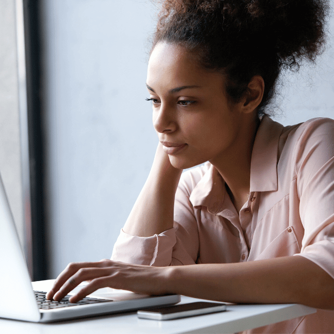 A Woman Is Sitting At A Table Using A Laptop Computer — Howells & Co Legal & Conveyancing In Cessnock, NSW