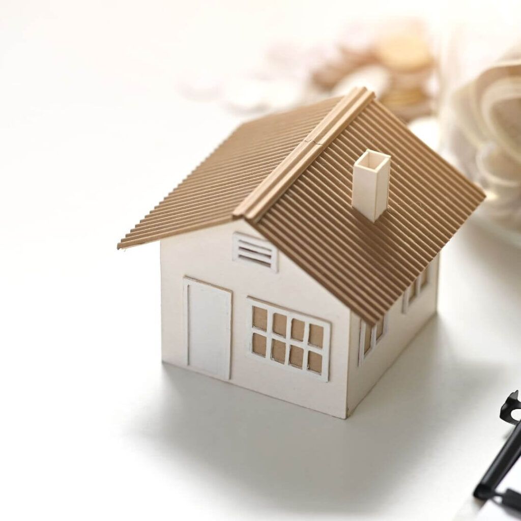 A Small Model House Is Sitting On A Table Next To A Cup Of Coffee And A Pen — Howells & Co Legal & Conveyancing In Cessnock, NSW