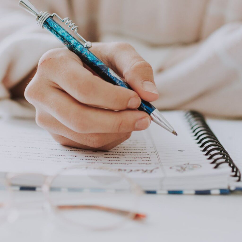 A Person Is Writing In A Notebook With A Blue Pen — Howells & Co Legal & Conveyancing In Cessnock, NSW