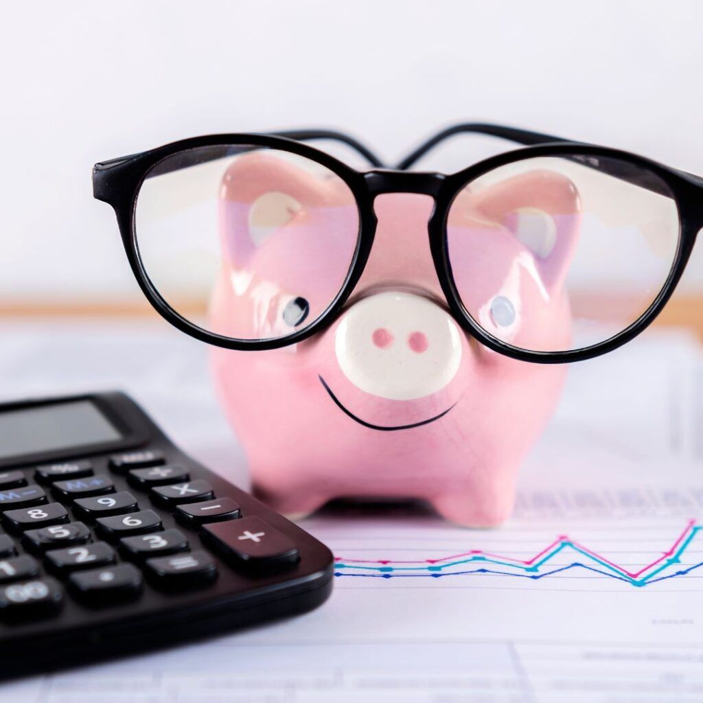 A Pink Piggy Bank Wearing Glasses Sits Next To A Calculator — Howells & Co Legal & Conveyancing In Cessnock, NSW