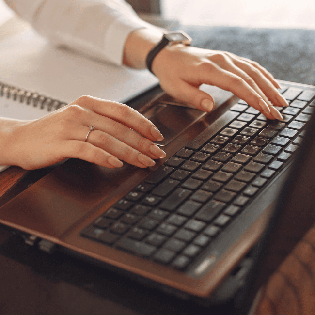 A Woman Is Typing On A Laptop With A Ring On Her Finger — Howells & Co Legal & Conveyancing In Cessnock, NSW
