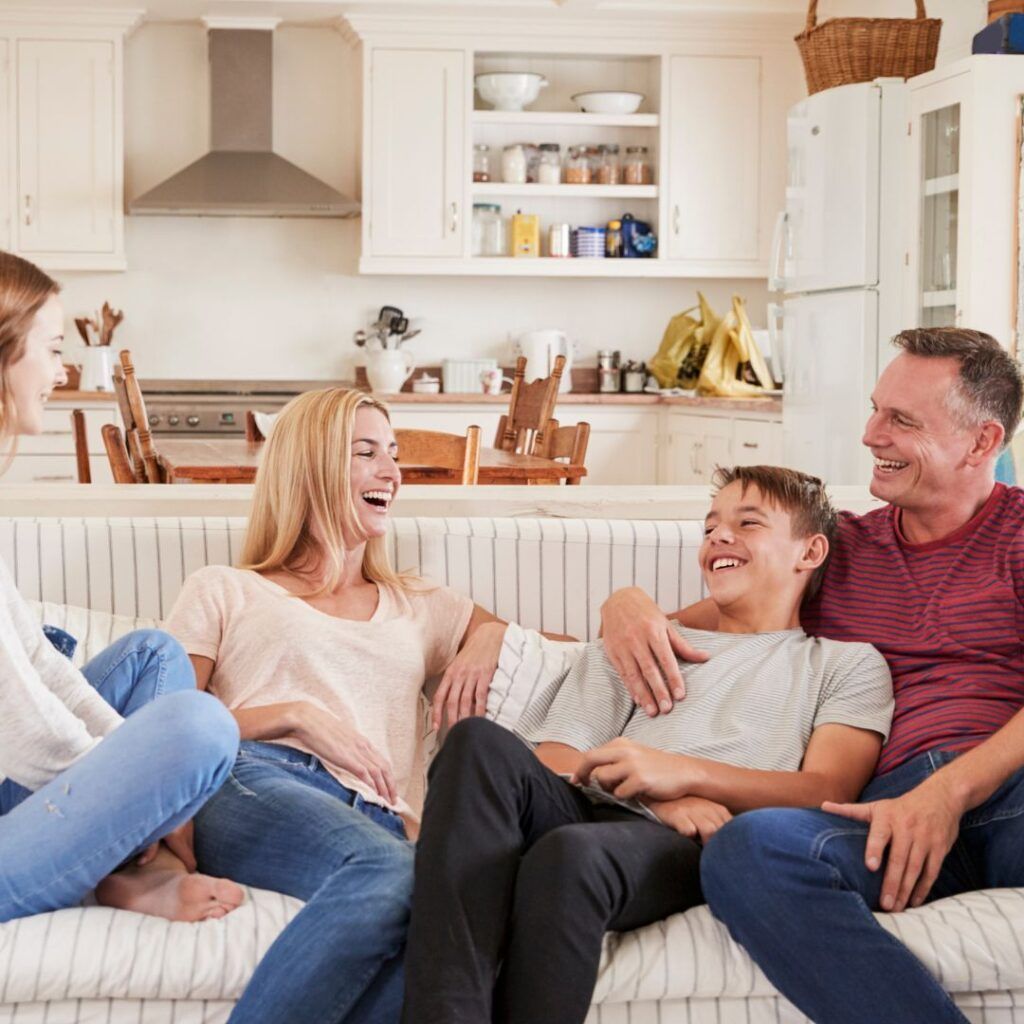 A Family Is Sitting On A Couch In A Living Room Laughing — Howells & Co Legal & Conveyancing In Cessnock, NSW