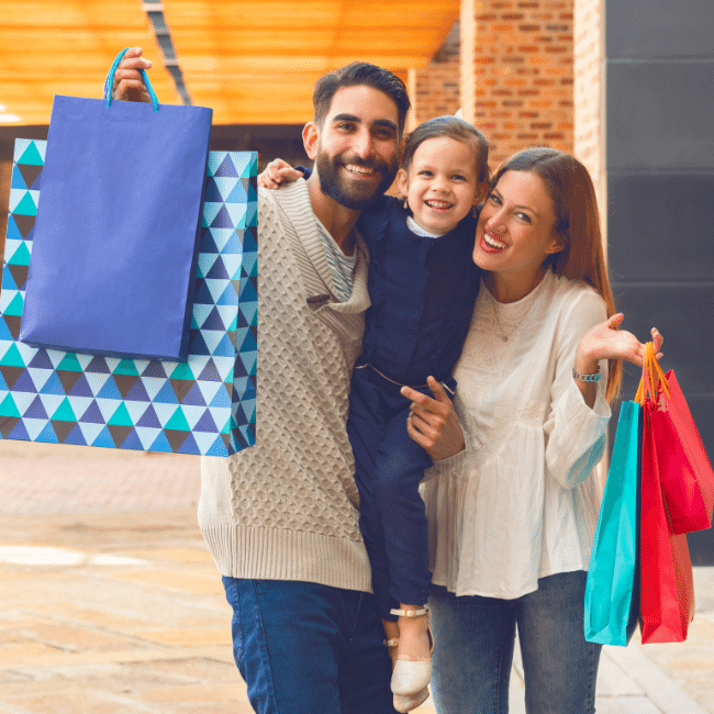 A Family Is Holding Shopping Bags And Posing For A Picture — Howells & Co Legal & Conveyancing In Cessnock, NSW