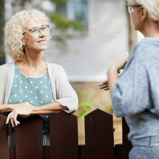 Two Women Are Talking Over A Wooden Fence — Howells & Co Legal & Conveyancing In Cessnock, NSW