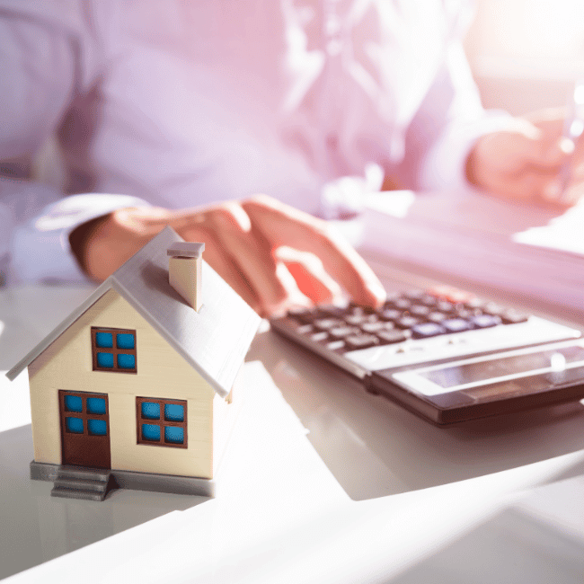 A Person Is Using A Calculator With A Small House In Front Of Them — Howells & Co Legal & Conveyancing In Cessnock, NSW
