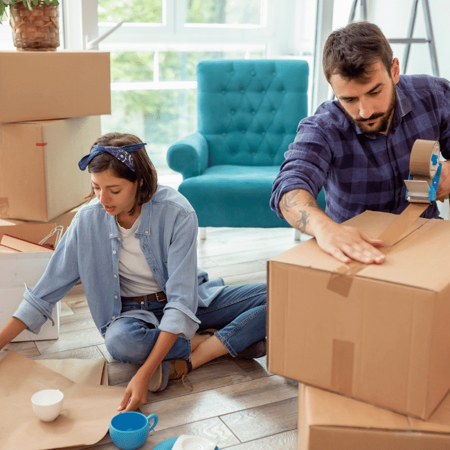 A Man And A Woman Are Sitting On The Floor Packing Boxes — Howells & Co Legal & Conveyancing In Cessnock, NSW