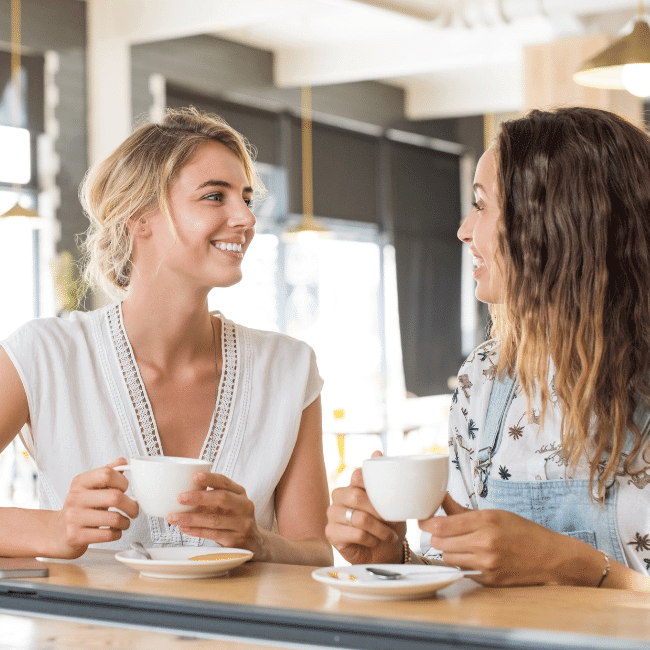 Two Women Are Sitting At A Table Drinking Coffee And Talking — Howells & Co Legal & Conveyancing In Cessnock, NSW