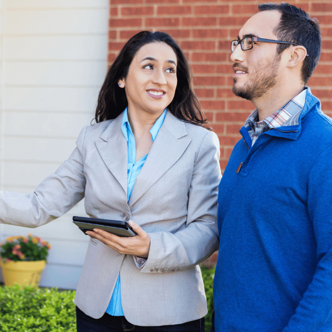 A Man And A Woman Are Standing In Front Of A Brick Building And The Woman Is Holding A Tablet — Howells & Co Legal & Conveyancing In Cessnock, NSW