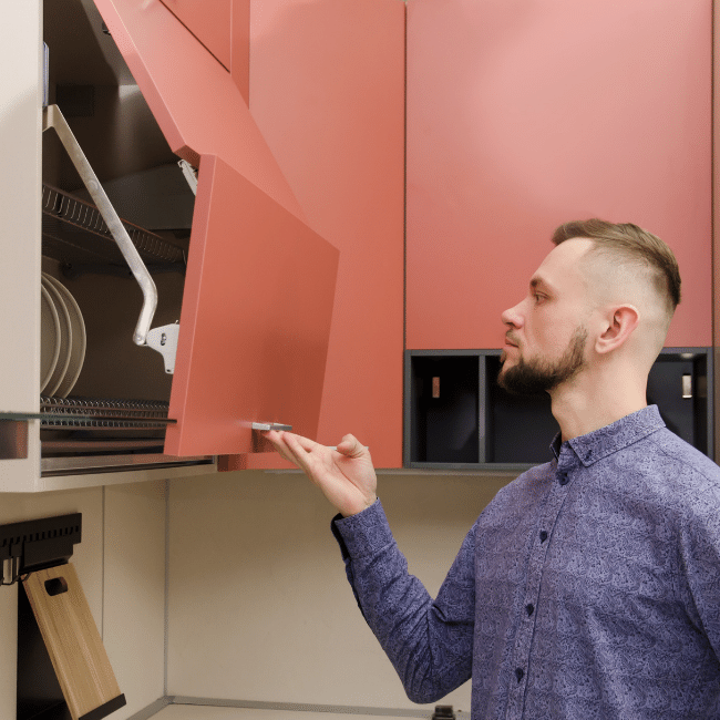 A Man In A Blue Shirt Is Opening A Red Cabinet In A Kitchen — Howells & Co Legal & Conveyancing In Cessnock, NSW