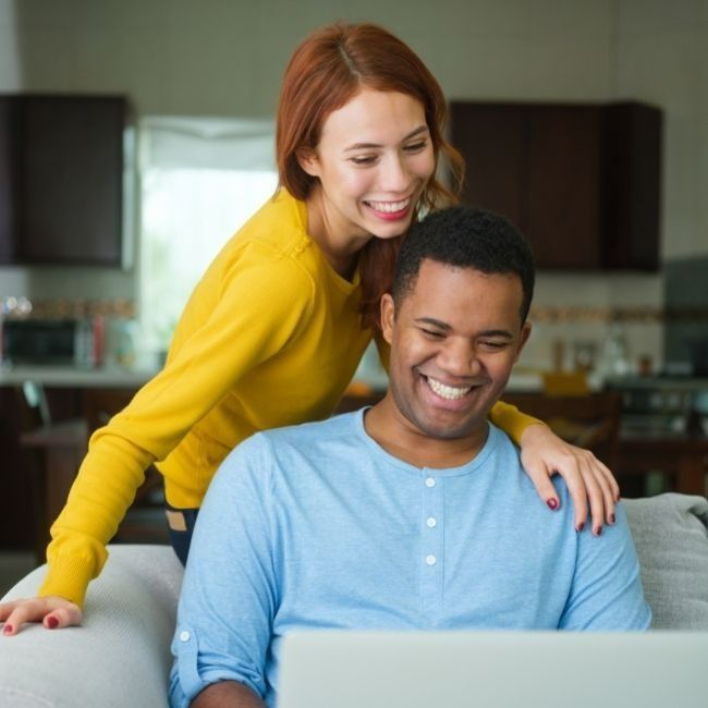 A Woman In A Yellow Sweater Stands Behind A Man Using A Laptop — Howells & Co Legal & Conveyancing In Cessnock, NSW