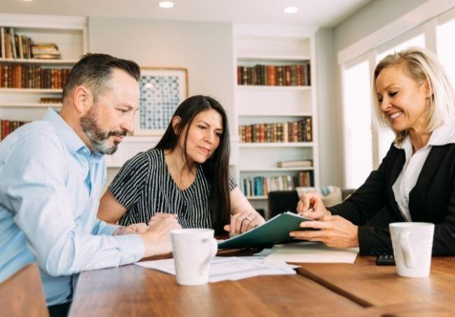 A Man And A Woman Are Sitting At A Table Looking At A Clipboard — Howells & Co Legal & Conveyancing In Lake Cessnock, NSW