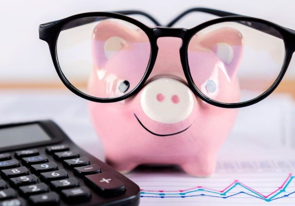 A Pink Piggy Bank Wearing Glasses Is Next To A Calculator — Howells & Co Legal & Conveyancing In Cessnock, NSW