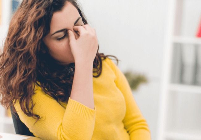 A Woman In A Yellow Sweater Is Covering Her Face With Her Hand — Howells & Co Legal & Conveyancing In Cessnock, NSW