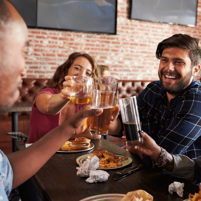 A Group Of People Are Sitting At A Table Toasting With Beer Glasses — Howells & Co Legal & Conveyancing In Cessnock, NSW
