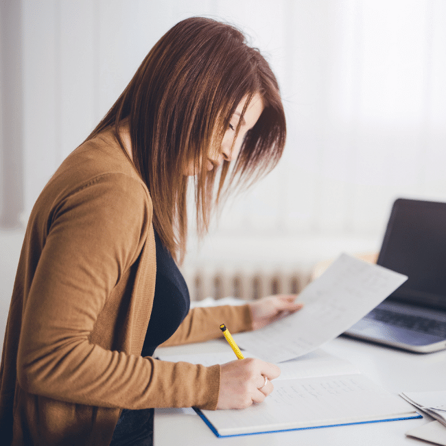 A Woman Is Sitting At A Desk Writing On A Piece Of Paper — Howells & Co Legal & Conveyancing In Cessnock, NSW