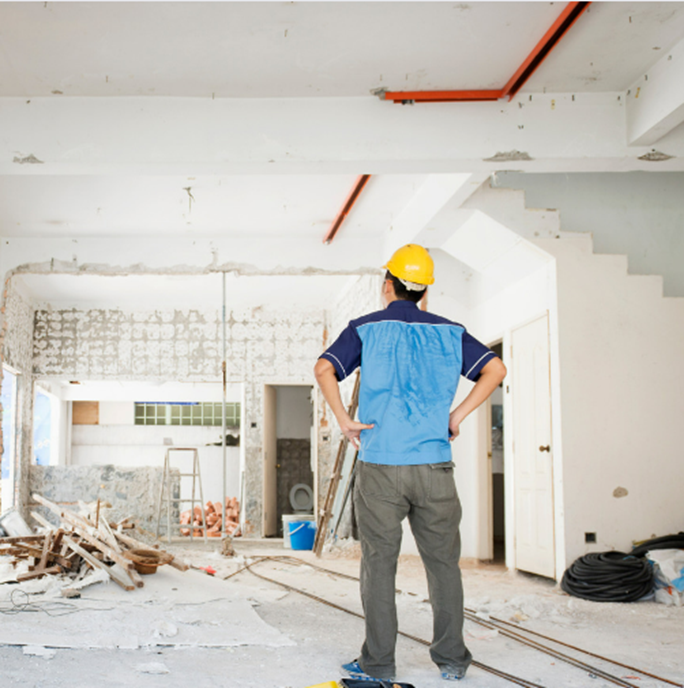 A Man Wearing A Hard Hat Is Standing In A Room Under Construction — Howells & Co Legal & Conveyancing In Cessnock, NSW