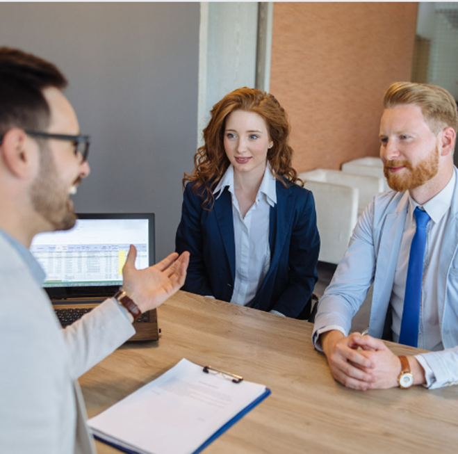 A Man And A Woman Are Sitting At A Table Talking To Each Other — Howells & Co Legal & Conveyancing In Cessnock, NSW