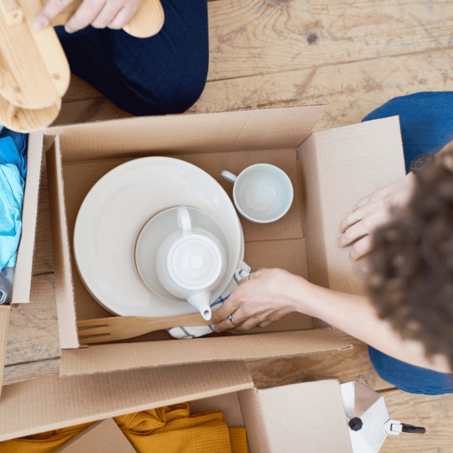 A Person Is Opening A Cardboard Box Filled With Plates And Cups — Howells & Co Legal & Conveyancing In Cessnock, NSW