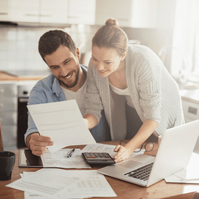 A Man And A Woman Are Sitting At A Table Looking At Papers And A Laptop — Howells & Co Legal & Conveyancing In Cessnock, NSW
