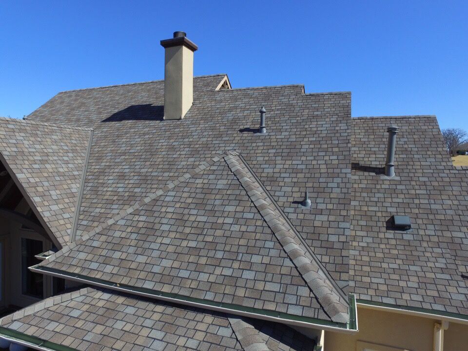 Overhead view of a house with a multi-tiered roof of gray shingles, a beige chimney, and a clear blue sky.