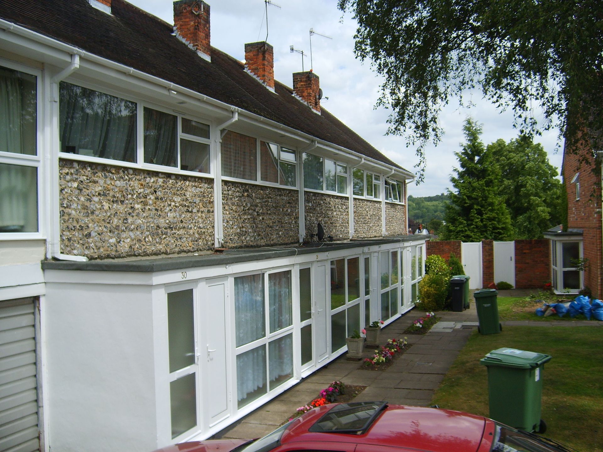Row of attached two-story houses with pebbledash siding and enclosed ground-floor porches, set on a residential street.