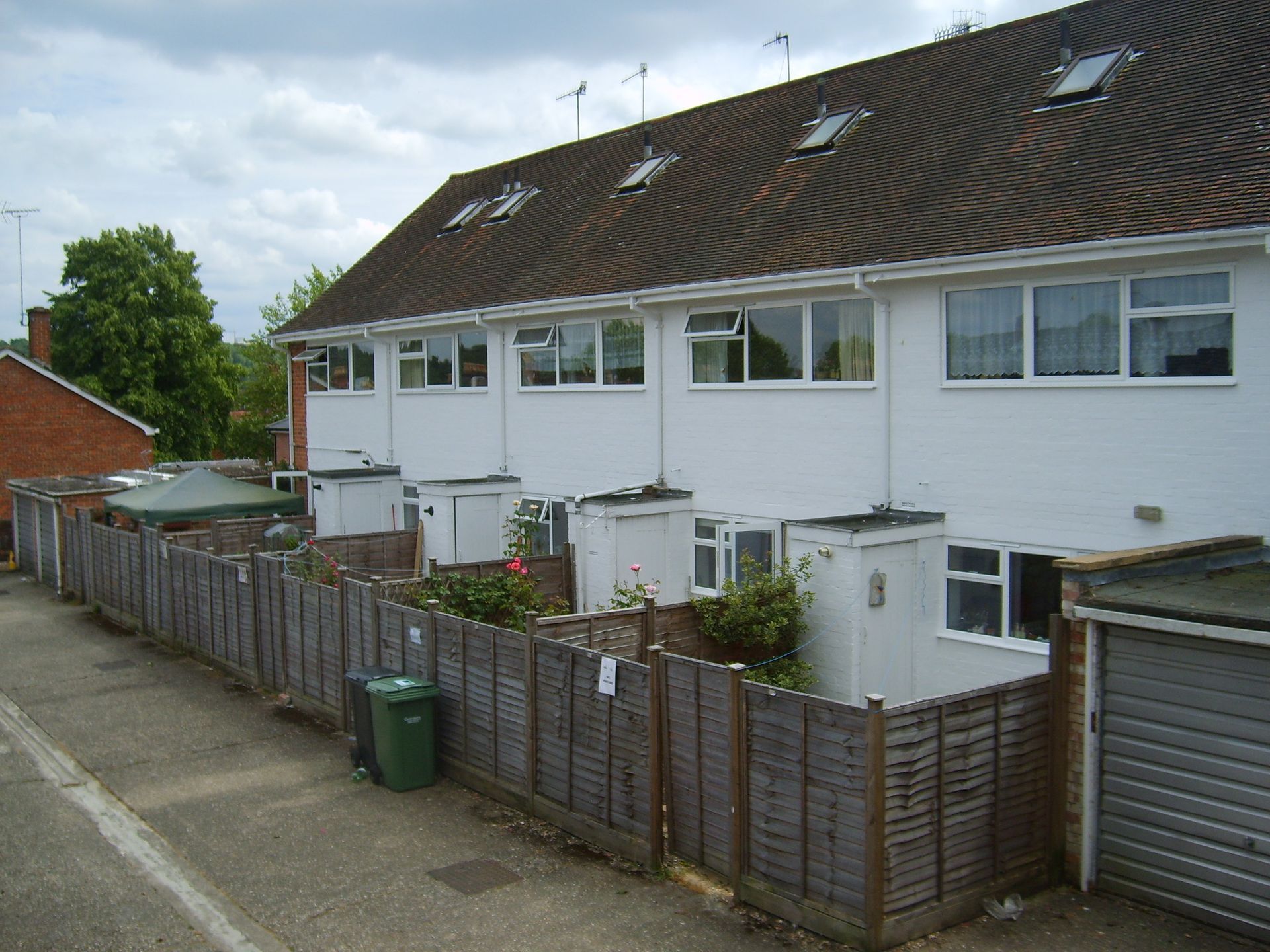 Row of white townhouses with wooden fences and small backyards; green bin in foreground.