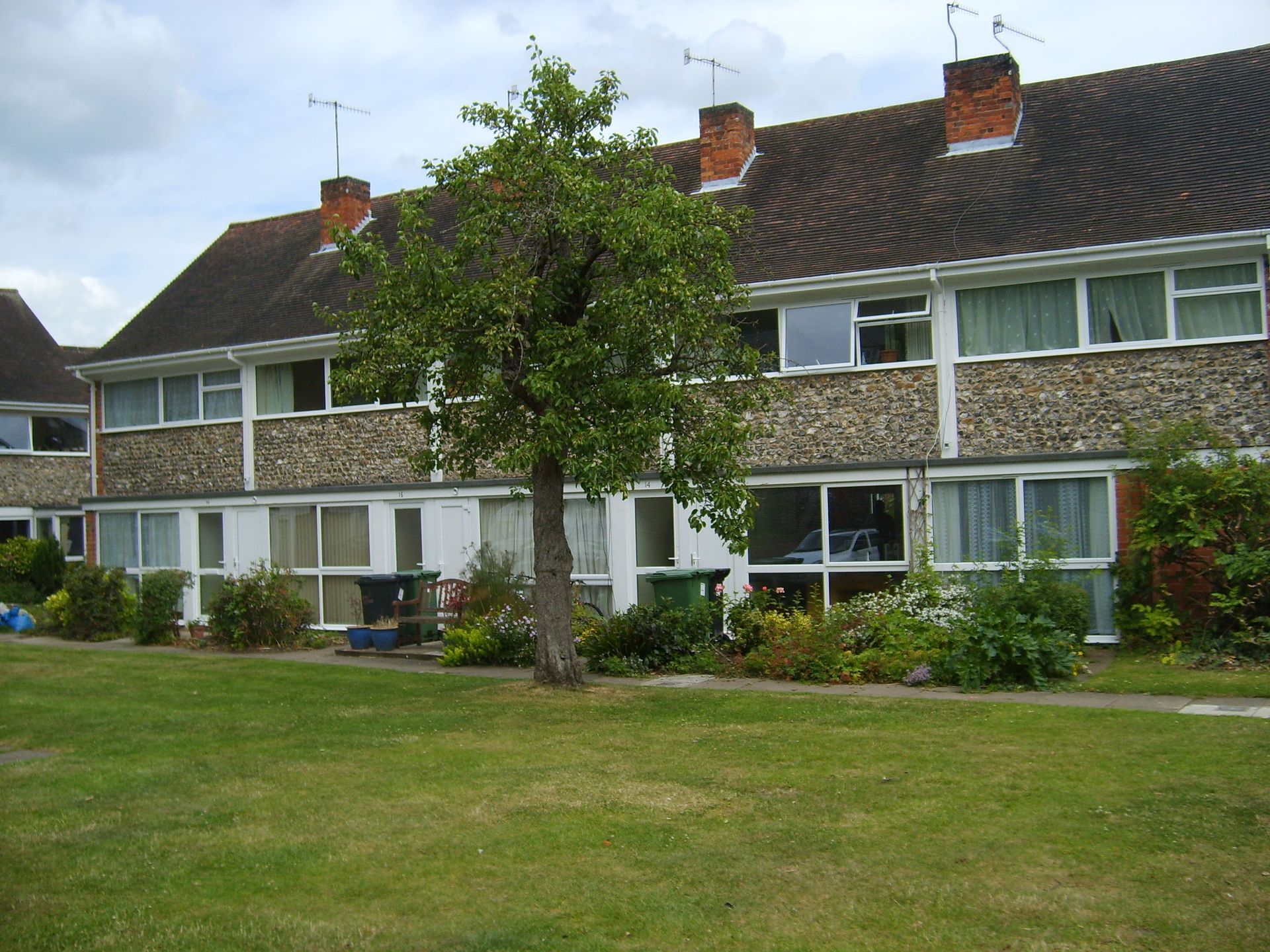 Row of two-story homes with gray tiled roofs and a small tree in front.  The facade is a mix of white and textured gray.