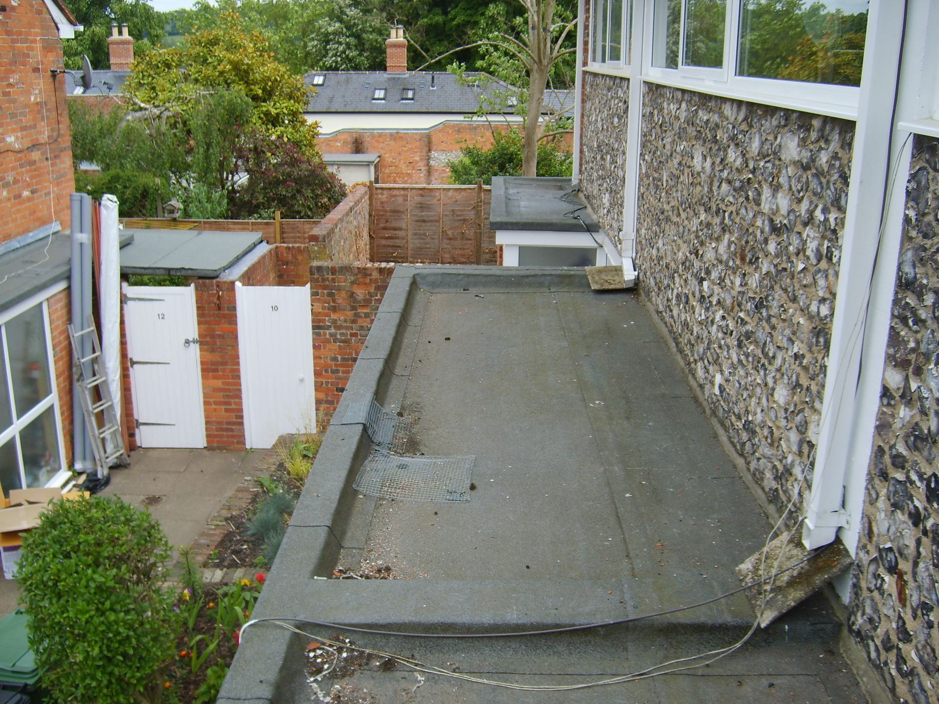 A flat, gray rooftop next to a speckled stone wall. In the background, a brick wall and white gate.