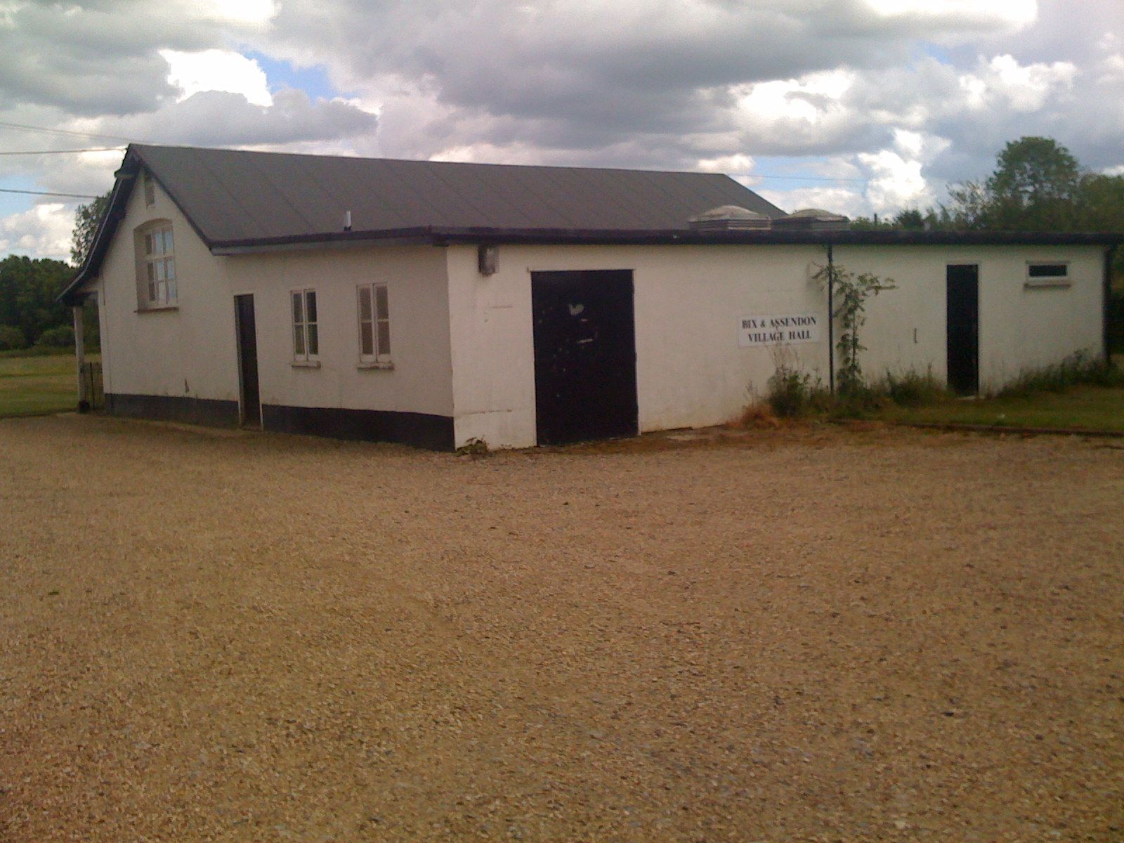 White building with a dark roof and doors. Gravel driveway in front under a cloudy sky.