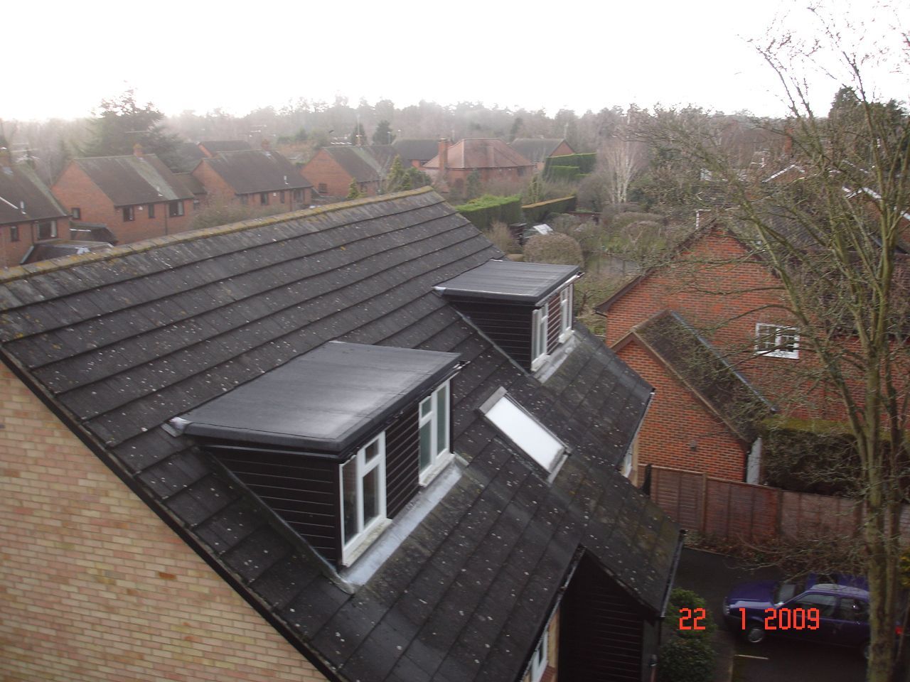 View of multiple houses with gray and reddish-brown tiled roofs and dormer windows. The sky is overcast.