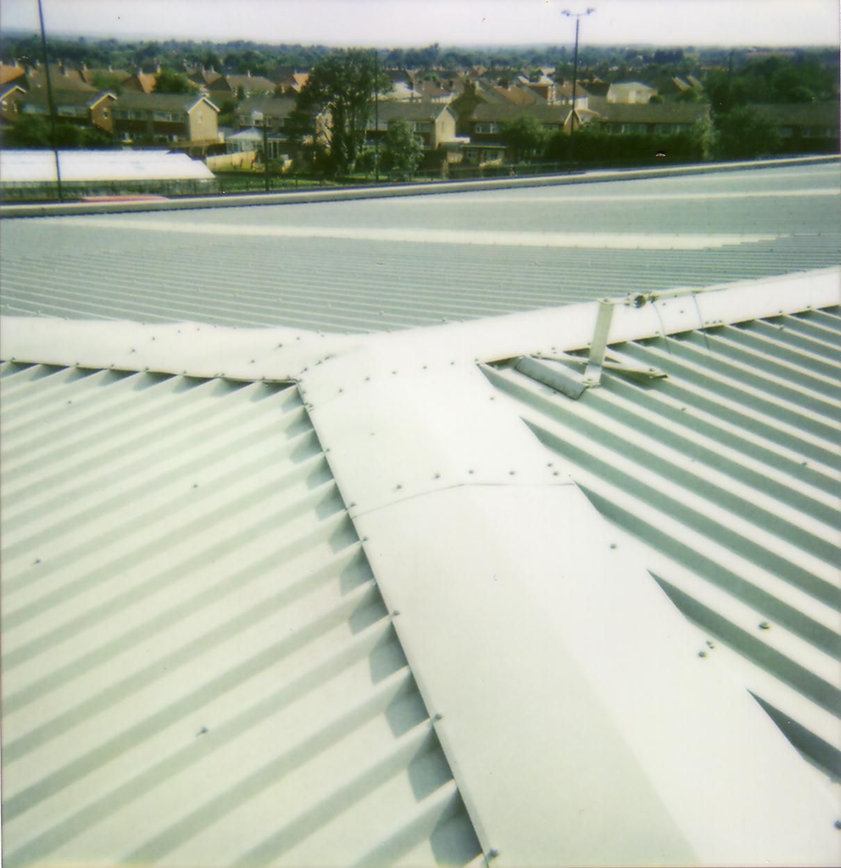 A metal roof with a white gutter system. Houses and trees are visible in the background.