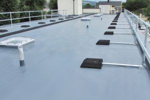 Flat, gray commercial roof with safety railings, vents, and equipment.
