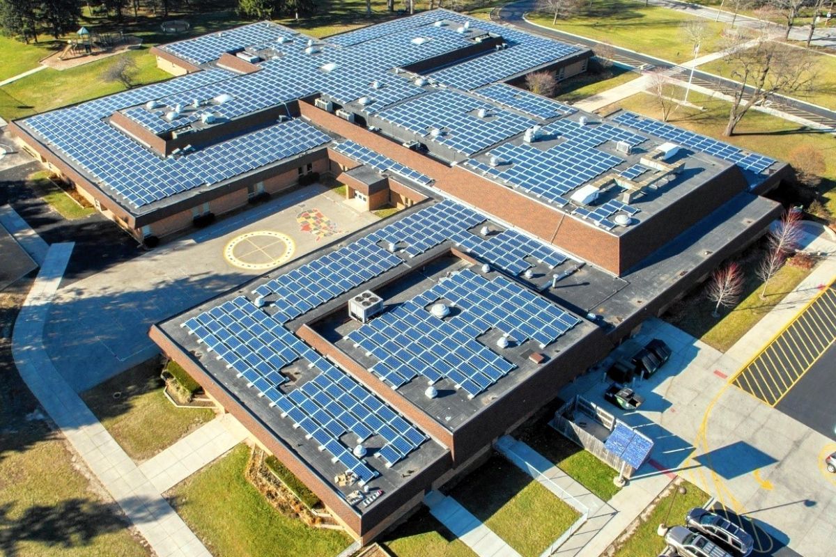 Aerial view of a school building covered with solar panels on its roof. A courtyard is visible in the center.